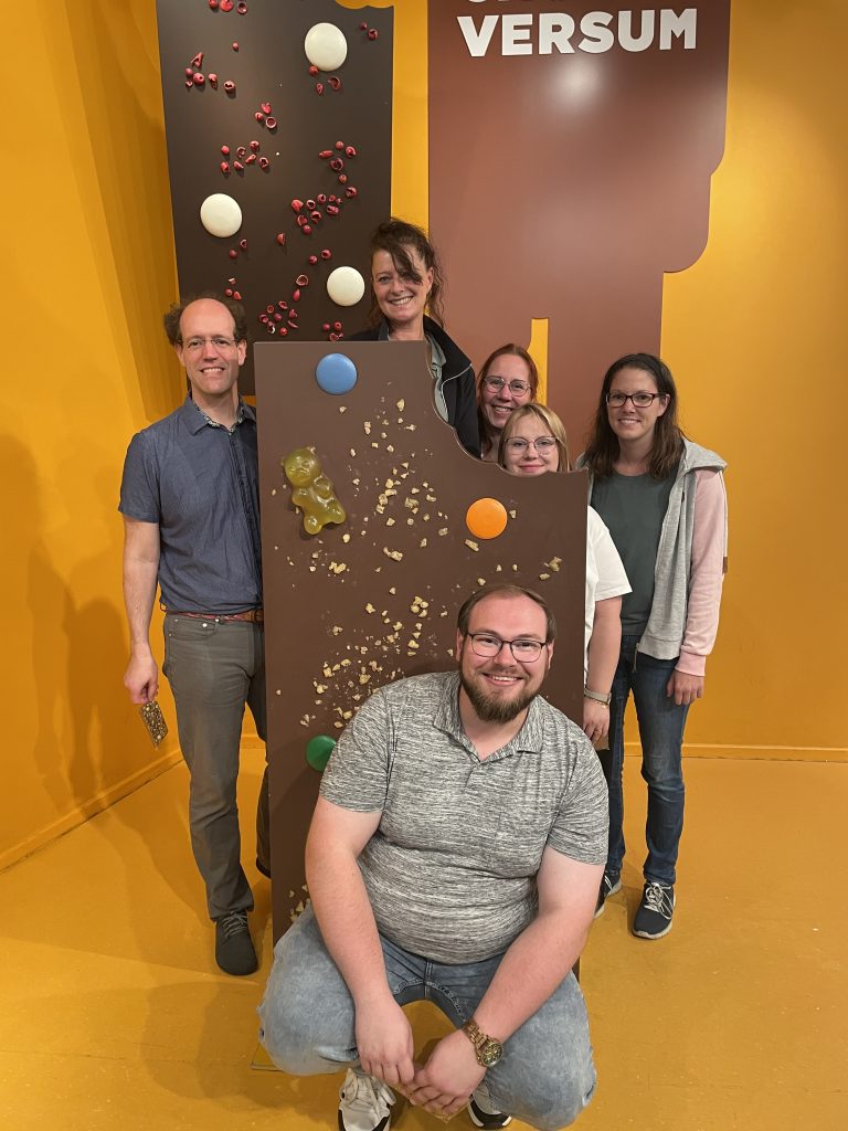 Unser Team im Chocoversum vor einer großen Schokoladentafel